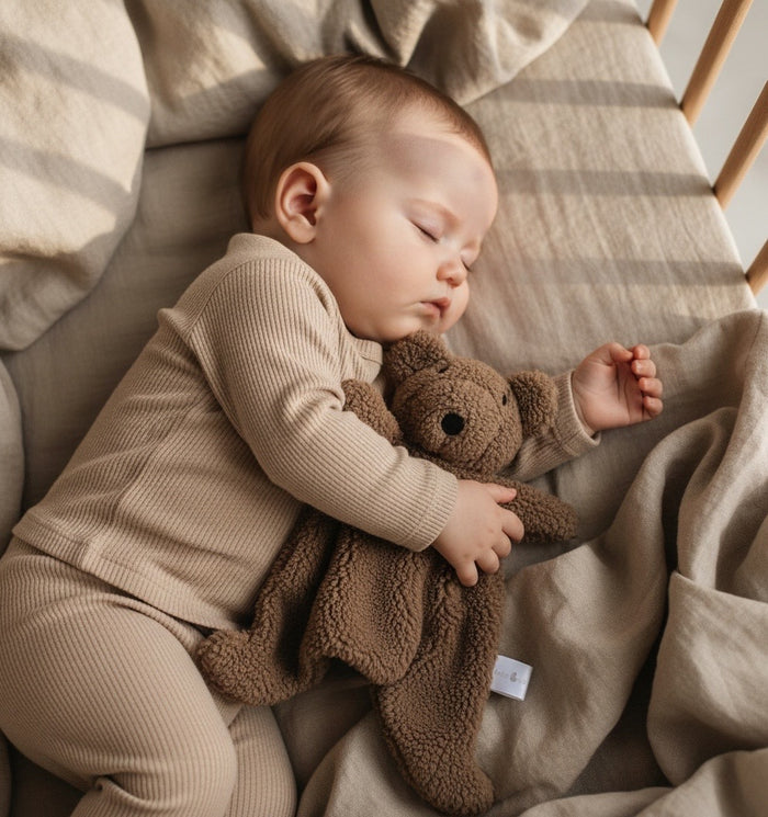 Baby sleeping with a brown teddy bear comforter on a soft surface