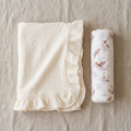 Folded white blanket with ruffled edge and owl printed swaddle on a beige surface