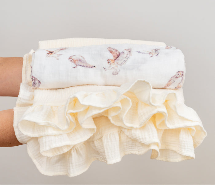 owl patterned swaddle rolled on top of a ruffled baby blanket held by a person against a neutral background